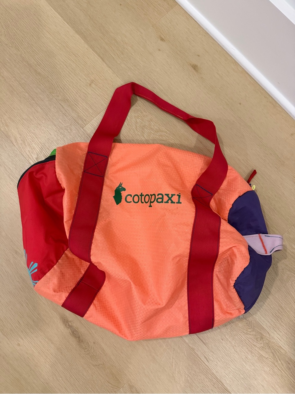 cotopaxi coral orange travel duffel with red straps and purple accents